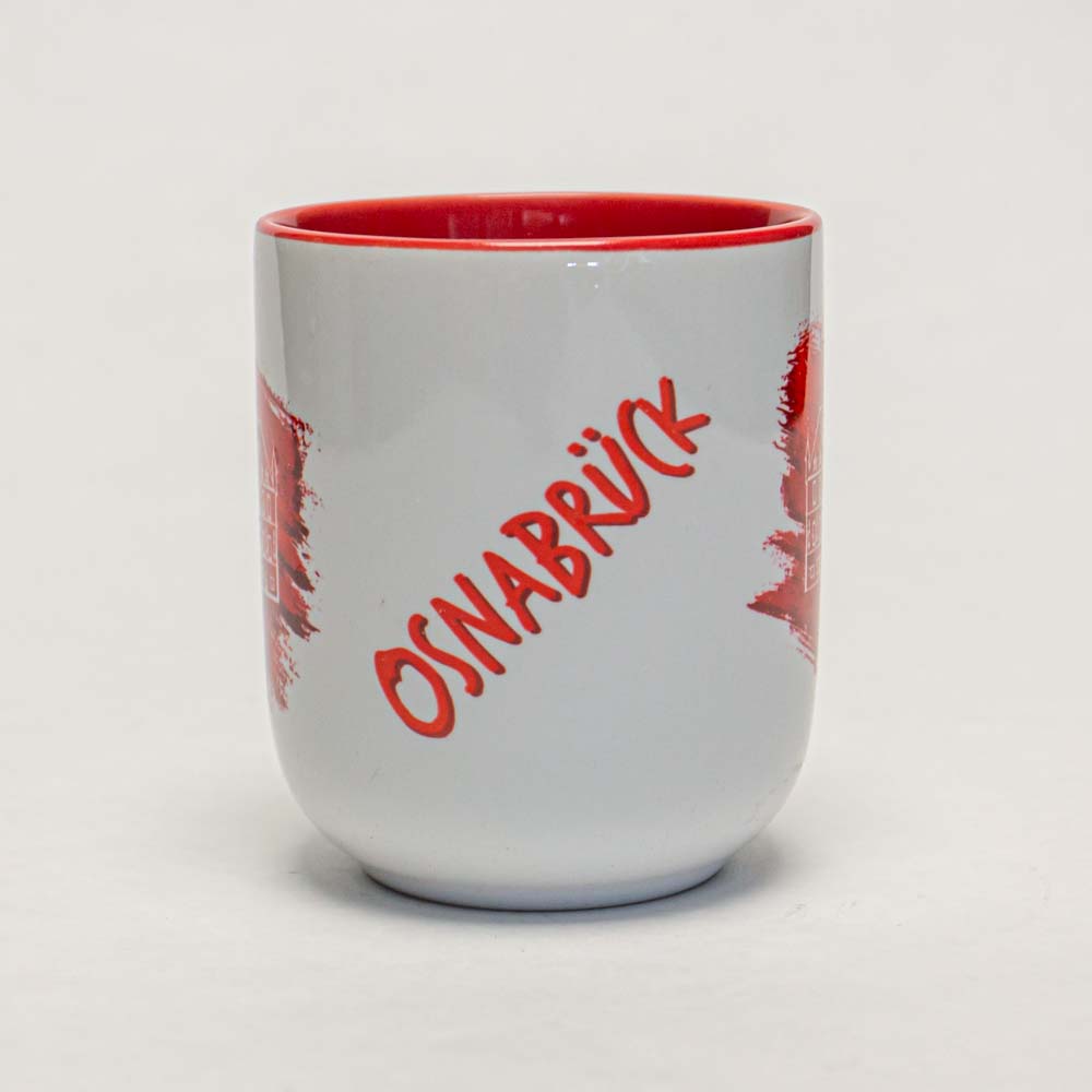 Die Tasse ist weiß mit roter Innenseite und hat das Wort "Osnabrück" in roter Schrift auf der Vorderseite. Das Design erinnert an einen Pinselstrich-Effekt rund um den Schriftzug.