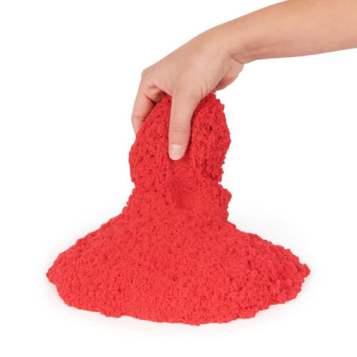 Eine Hand hält eine Masse aus rotem formbarem Sand. Der Sand sieht weich und leicht formbar aus.
