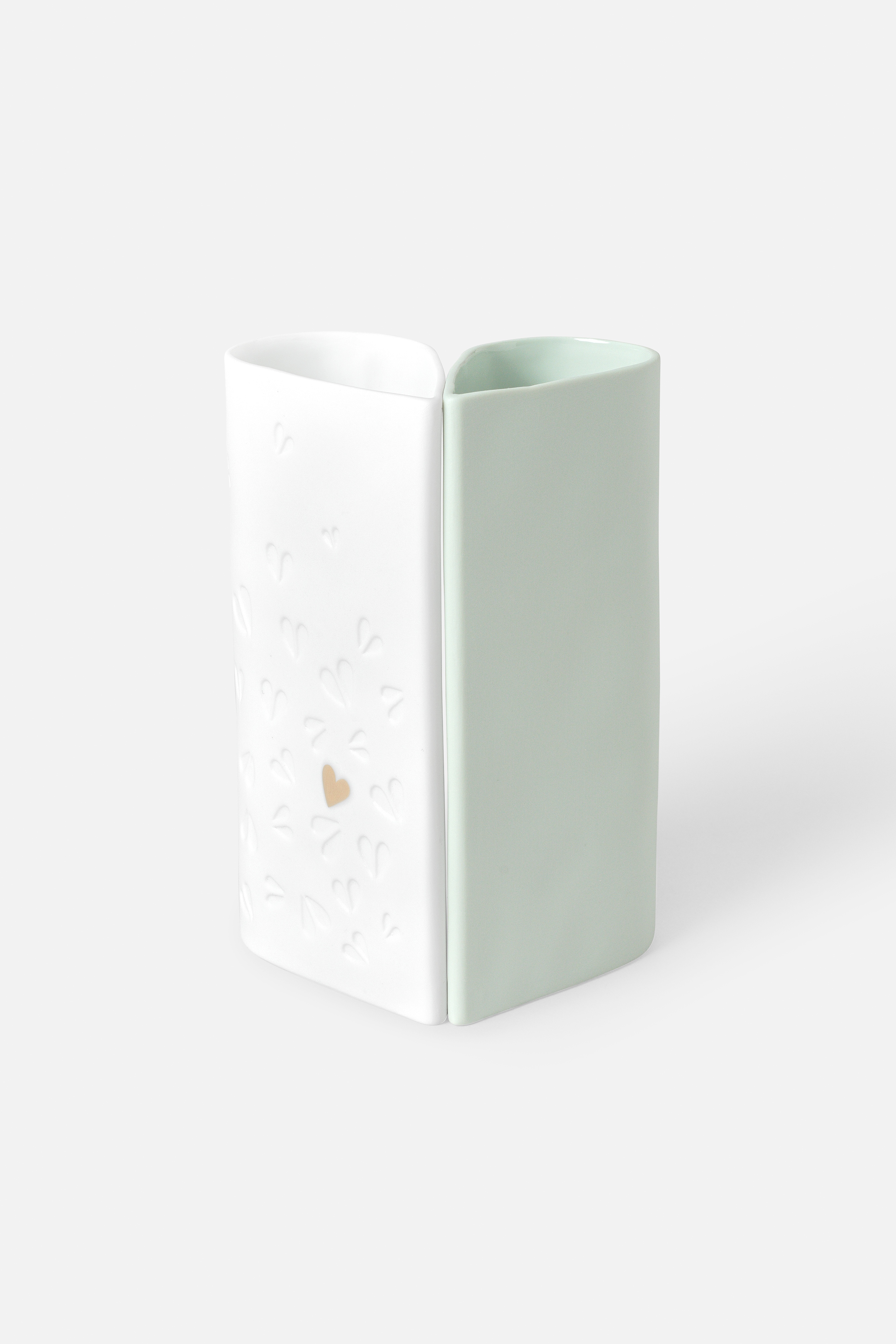 Das Bild zeigt eine zweiteilige Vase in Herzform, wobei eine Hälfte weiß mit eingravierten kleinen Herzen und die andere Hälfte hellgrün ist. Auf der weißen Seite befindet sich ein kleines goldenes Herz.