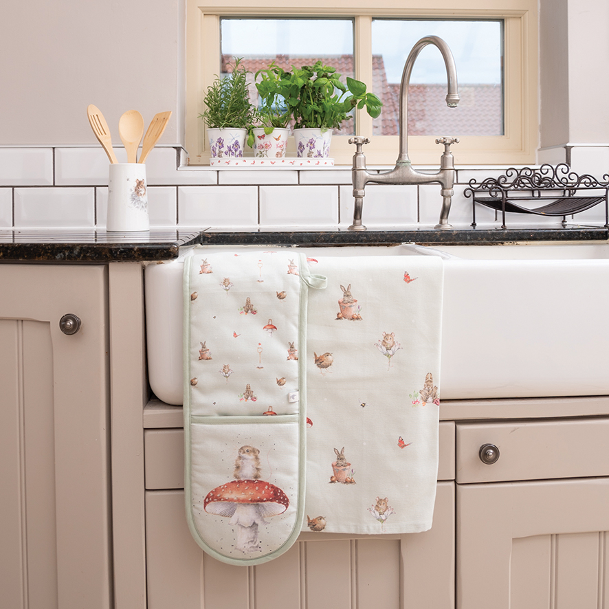 Auf dem Bild ist ein Küchentuch mit dem Namen „Küchentuch Gartenfreunde“ zu sehen, das süße Gartenmotive wie Kaninchen und Pilze zeigt. Das Tuch hängt dekorativ über die Küchenspüle in einer freundlich eingerichteten Küche.