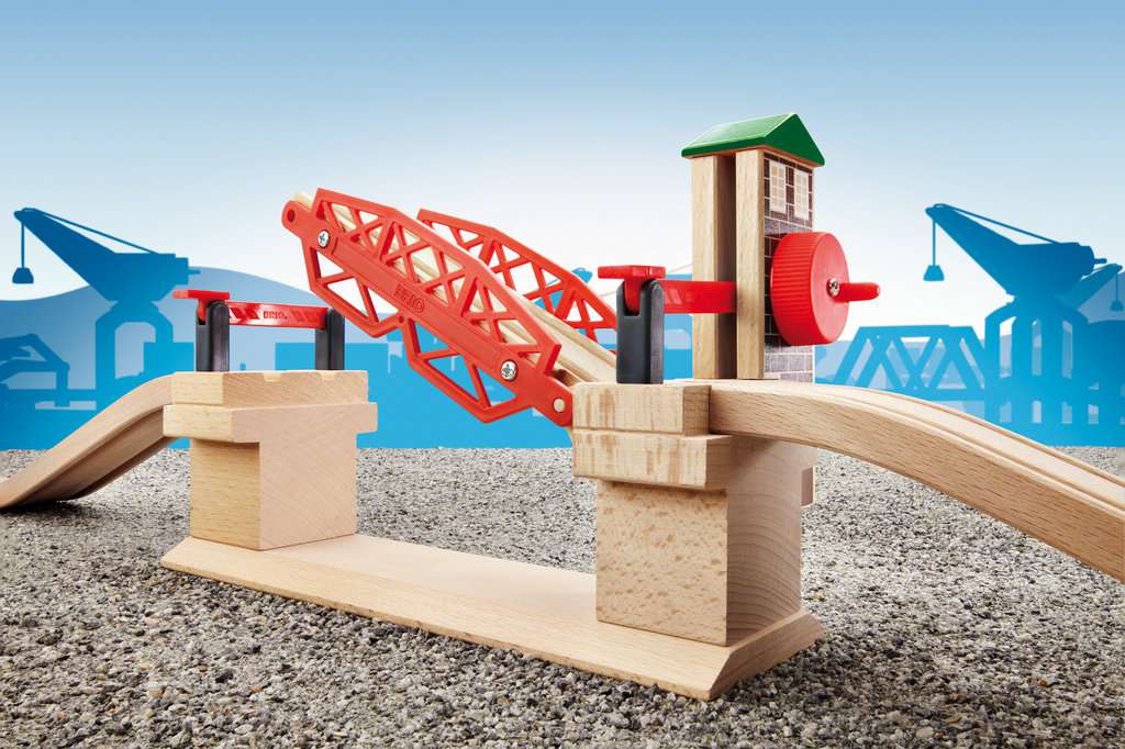 Das Bild zeigt die BRIO® Hebebrücke 33757, eine rote Zugbrücke aus Holz. Sie gehört zu einem Spielzeug-Eisenbahnset und steht auf einem steinähnlichen Untergrund.