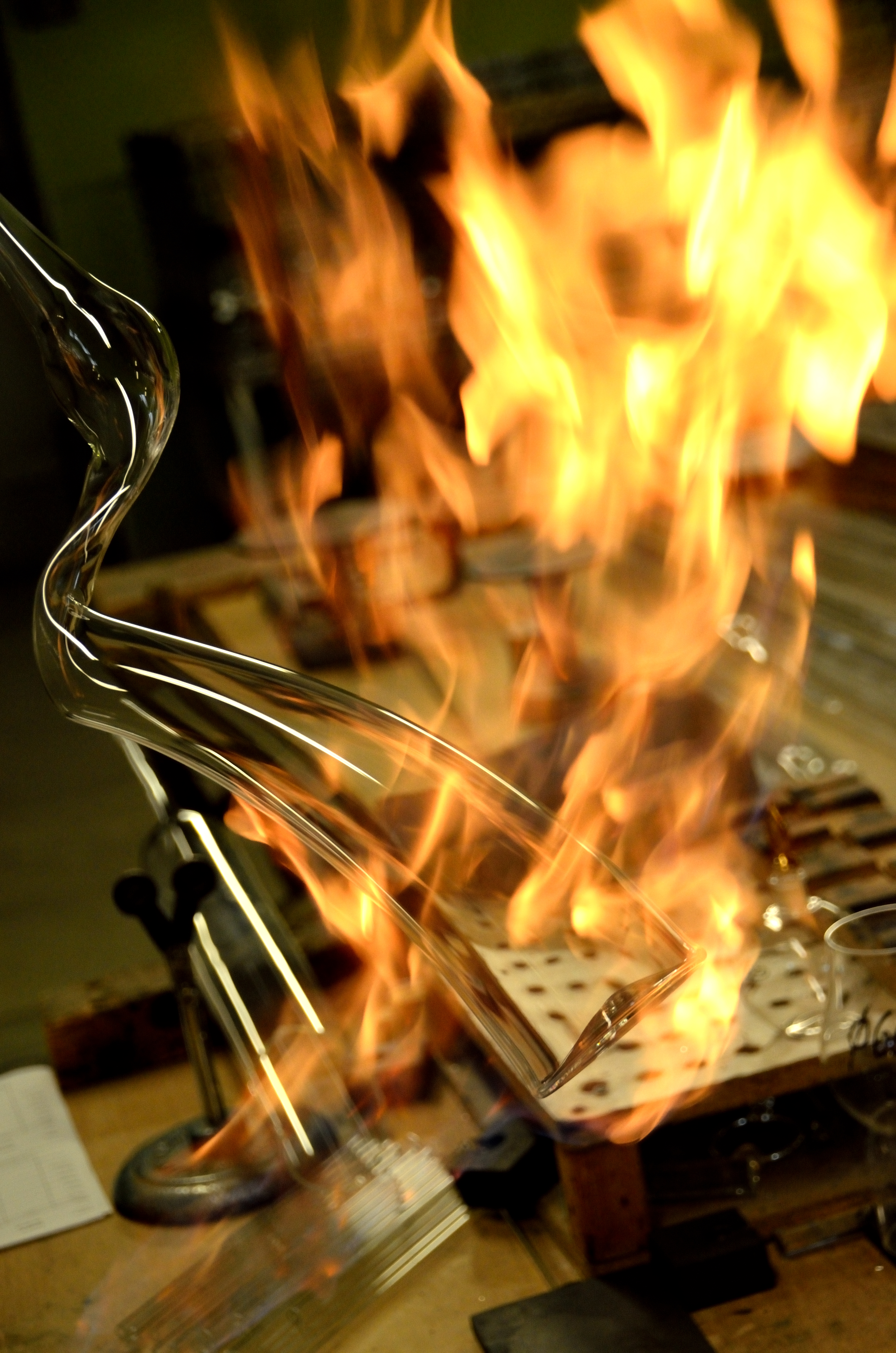 Ein Glasrohr wird mit einer offenen Flamme erhitzt und geformt. Die Flammen umgeben das Glas und sorgen für eine intensive Hitzeeinwirkung.