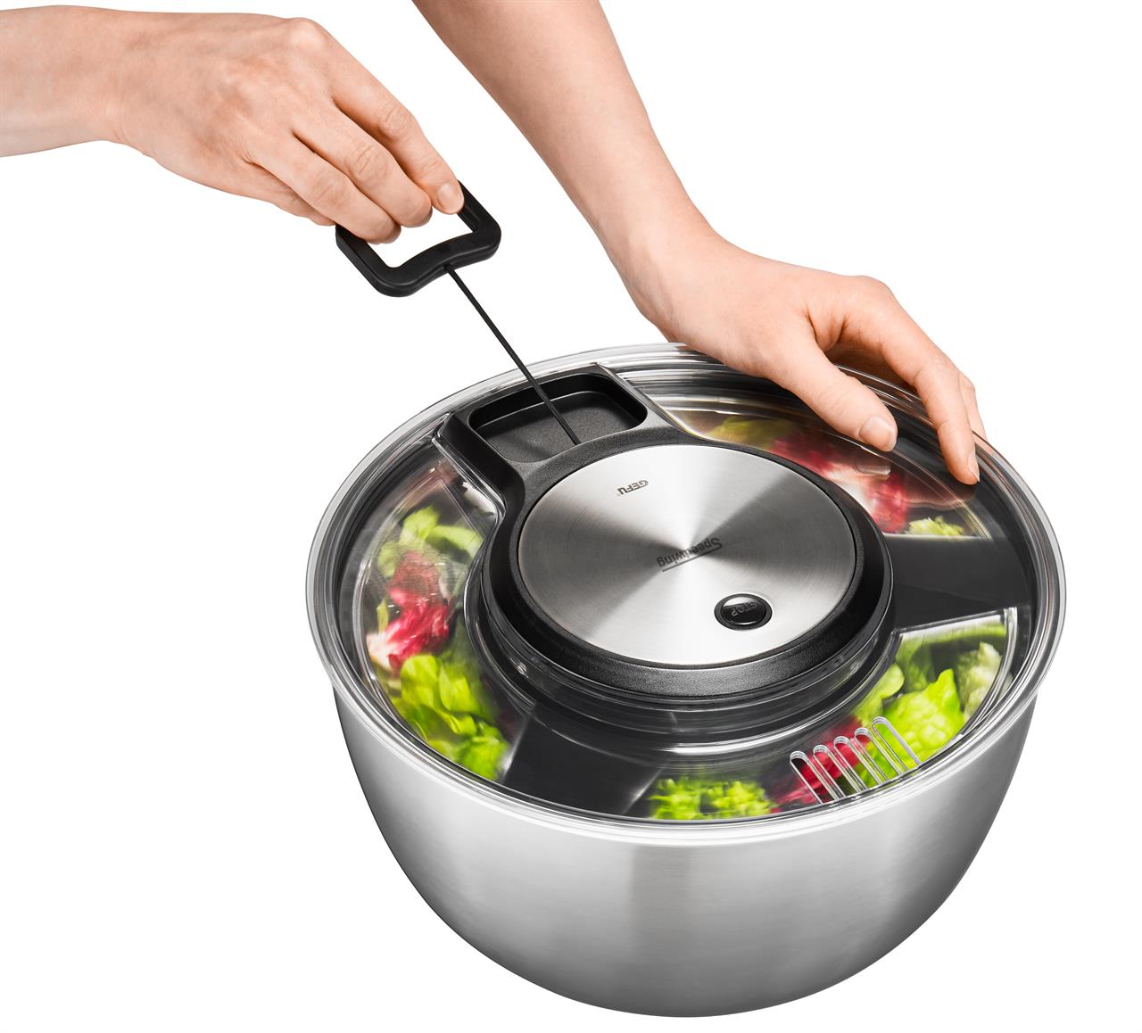 Das Bild zeigt eine Salatschleuder SPEEDWING® aus Edelstahl. Eine Person bedient die Schleuder mit einer Hand an der Kurbel und hält mit der anderen Hand den Deckel fest.