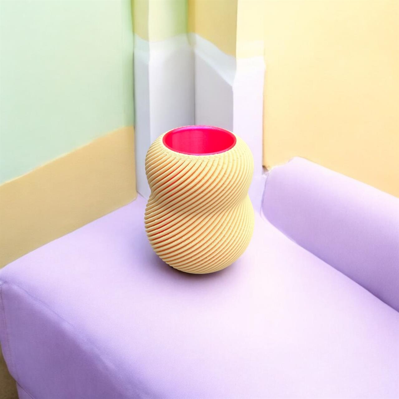Das Bild zeigt eine dekorative Vase mit dem Namen "Vase Bloom 100% Vanilla". Die Vase hat eine gewundene, gelbe Außenstruktur und ein leuchtend pinkes Inneres.