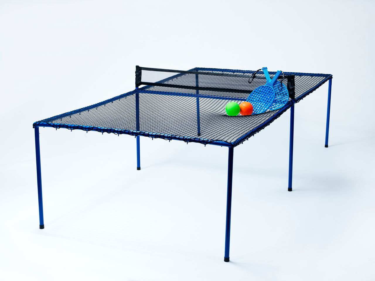 Auf dem Bild ist ein "Bounce Ping Pong Tisch" zu sehen, der aus einem Netz und blauen Beinen besteht. Auf dem Tisch liegen zwei Schläger und zwei bunte Bälle.