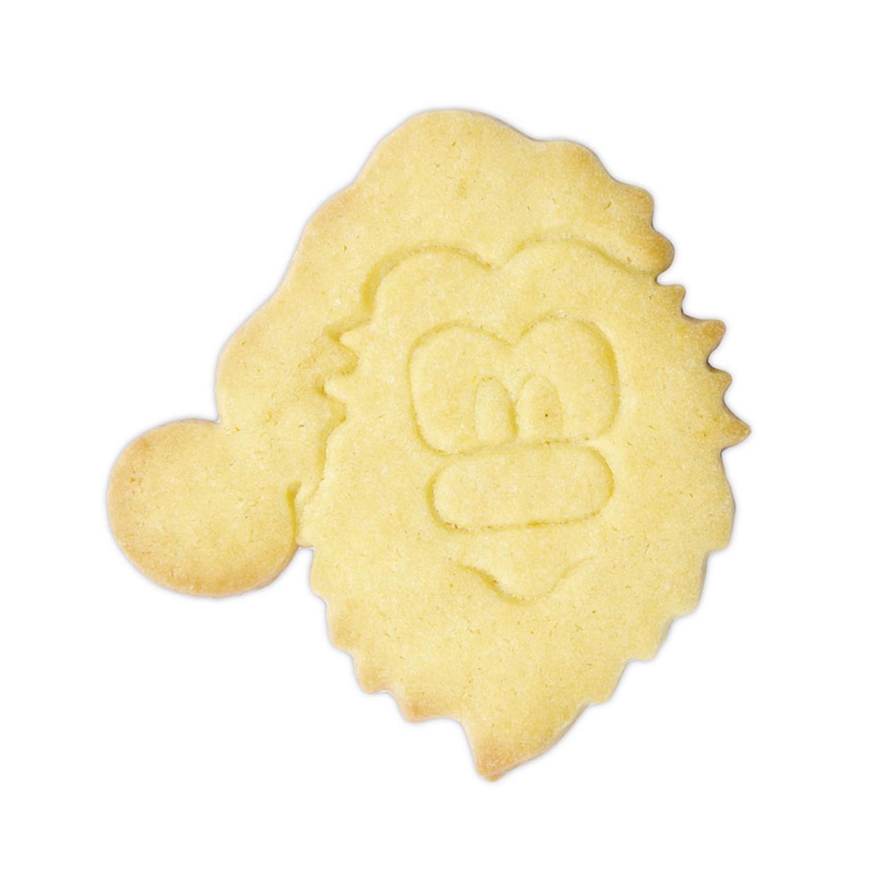 Auf dem Bild ist ein Keks in Form eines Nikolausgesichts zu sehen. Der Keks wurde mit einem Ausstecher gemacht und zeigt die Konturen von Bart, Mütze und Gesicht.