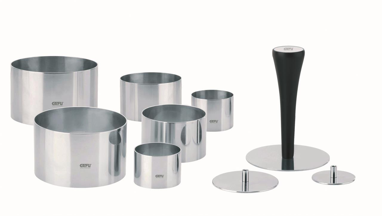 Das Bild zeigt das Produkt "Profispeisenringe Formidable, 10-Tlg." aus Edelstahl. Es besteht aus mehreren verschieden großen Ringen und einem schwarzen Stößel zum Formen und Anrichten von Speisen.