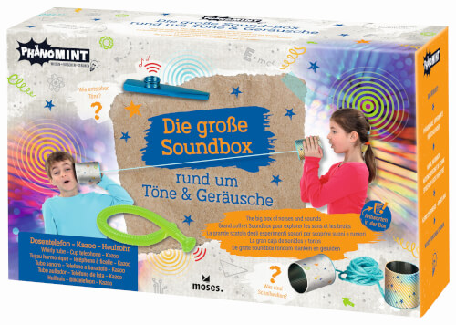 Auf dem Bild ist eine bunte Spielzeug-Box mit dem Titel „Die große Soundbox – rund um Töne & Geräusche“ zu sehen. Zwei Kinder spielen mit Dosen und einer Schnur, um Geräusche zu machen.