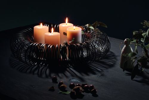 Die Caracas Adventschale besteht aus pulverbeschichtetem Stahldraht in Antik-Braun. In der Schale stehen vier brennende Kerzen, umgeben von dekorativen Zweigen.