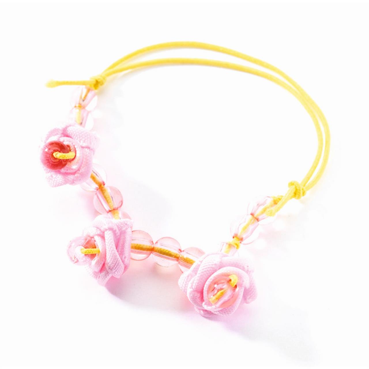 Auf dem Bild ist ein selbstgemachtes Armband zu sehen. Es besteht aus rosa Perlen und drei rosa Stoffblumen, die auf einem gelben Faden aufgefädelt sind.