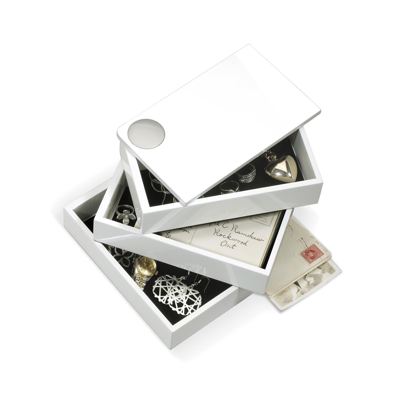 Die Abbildung zeigt eine weiße Spindle Aufbewahrungsbox mit mehreren übereinander drehbaren Fächern. In den Fächern befinden sich Schmuckstücke, Briefe und andere kleine Gegenstände.