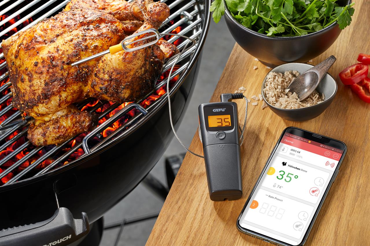 Ein Grill- und Bratenthermometer CONTROL, 1 Kanal, misst die Temperatur eines grillenden Hähnchens. Die Temperatur wird digital am Gerät und auf einem Smartphone angezeigt.