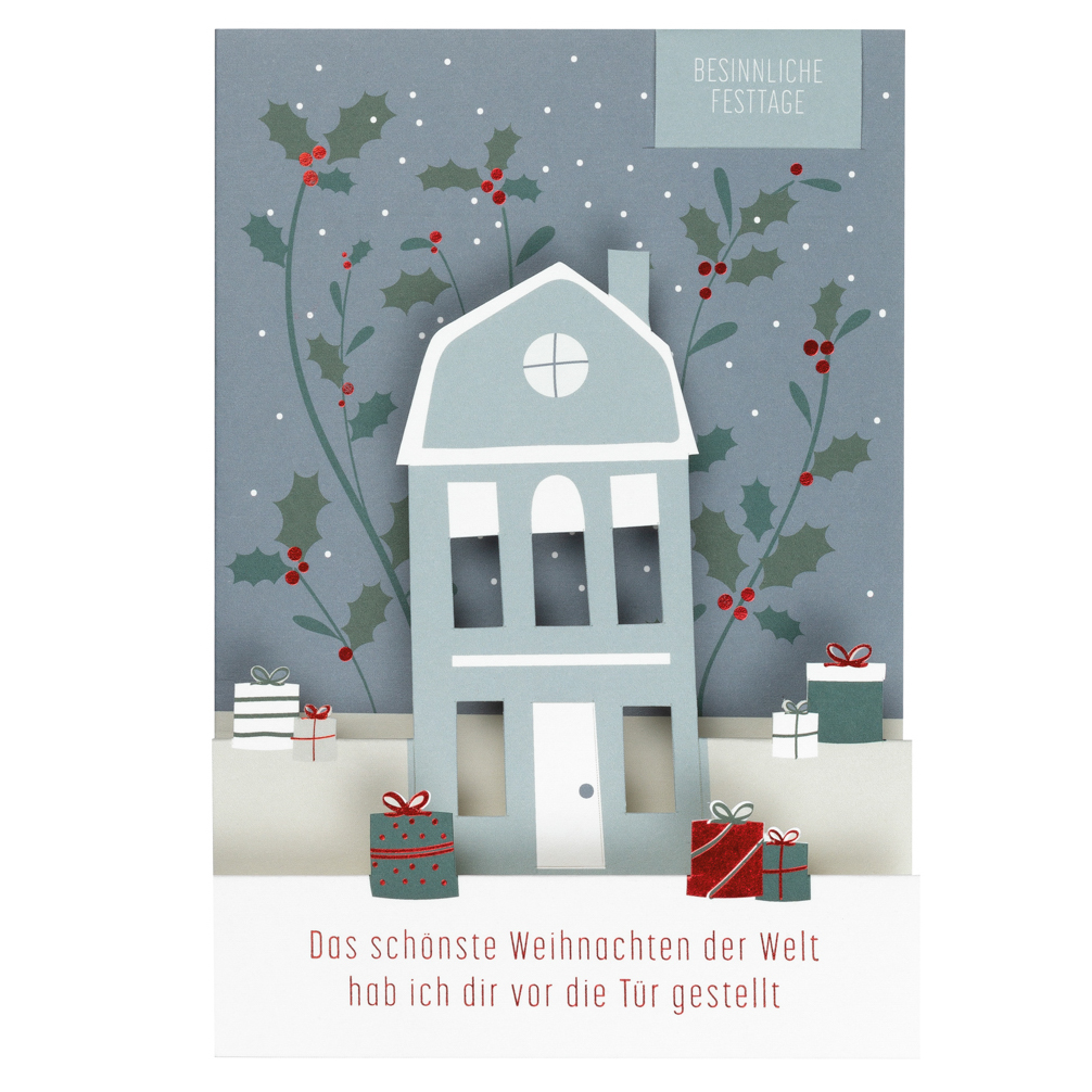 Die Karte zeigt ein stilisiertes Haus mit Geschenken davor und Stechpalmenzweigen im Hintergrund. Oben steht "Besinnliche Festtage" und unten steht "Das schönste Weihnachten der Welt hab ich dir vor die Tür gestellt."