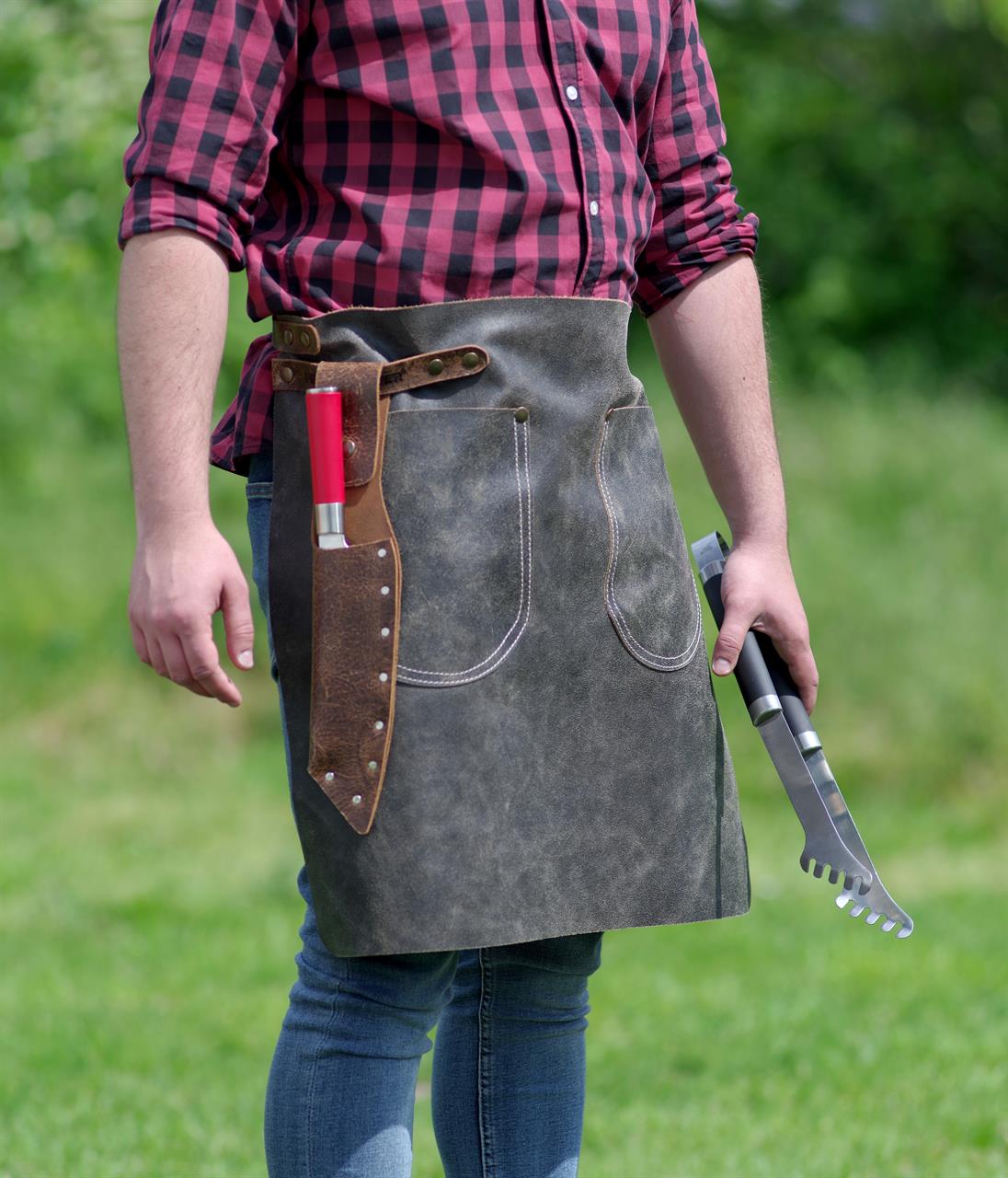 Die Abbildung zeigt eine Person mit einer anthrazitfarbenen Hüftschürze aus Antikleder in der Größe 2 (70x55 cm). Die Schürze hat praktische Taschen und eine Halterung für Grillbesteck oder Messer.