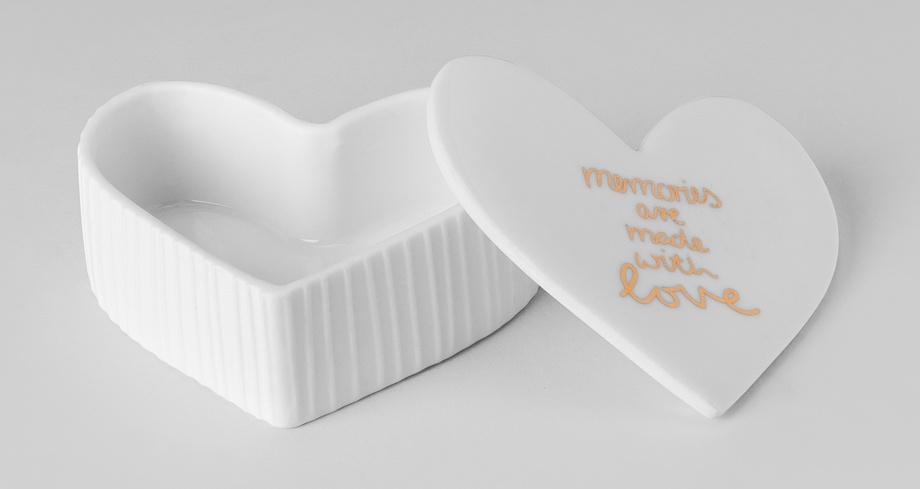 Auf dem Bild ist eine kleine, weiße Herzdose mit abgenommenem Deckel zu sehen. Auf dem Deckel steht in orangefarbener Schrift: "memories are made with love".