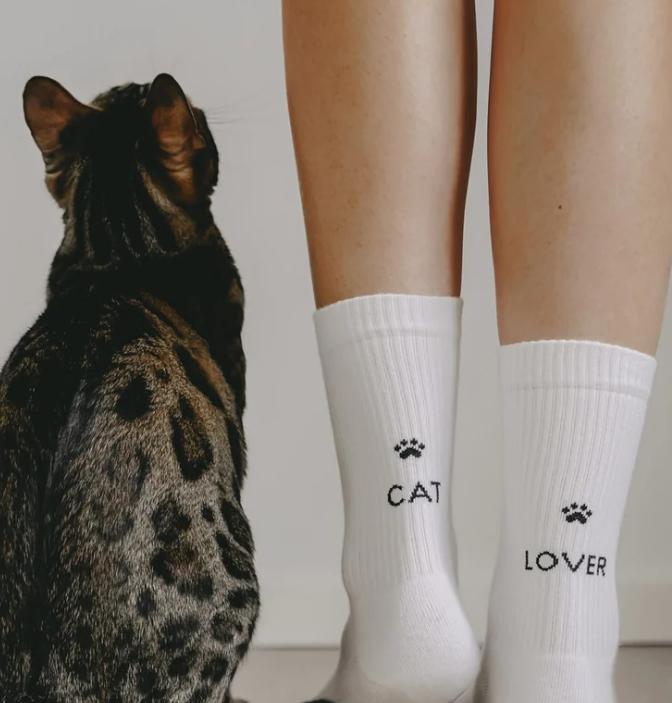 Das Bild zeigt weiße Socken mit 'Cat Lover'-Motiv in Größe S. Das Design ist besonders für Freunde von Katzen gemacht.