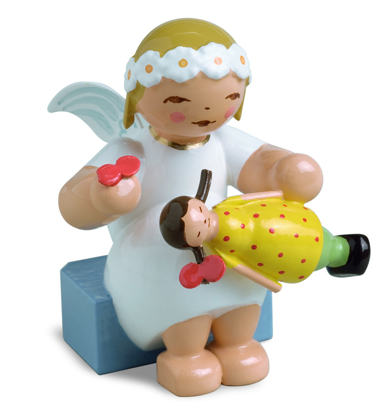 Das Bild zeigt einen Margeritenengel, sitzend, mit Puppe. Der Engel ist liebevoll gestaltet und hält eine kleine Puppe in der Hand.