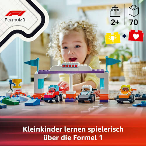 Ein kleines Kind spielt mit bunten Formel 1 Bausteinen auf dem Boden. Im Vordergrund sind mehrere Rennwagen und ein Starttor aufgebaut.