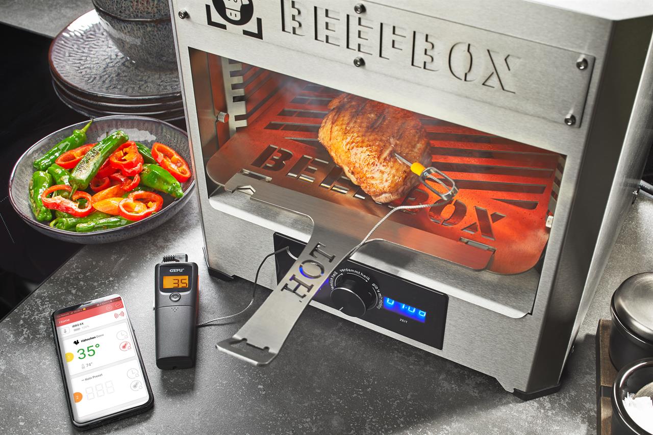 Das Bild zeigt einen Grill mit einem Bratenthermometer CONTROL, 1 Kanal, das in ein Stück Fleisch gesteckt ist. Neben dem Grill liegt ein digitales Thermometer und ein Smartphone, beide zeigen die Temperatur von 35°C an.