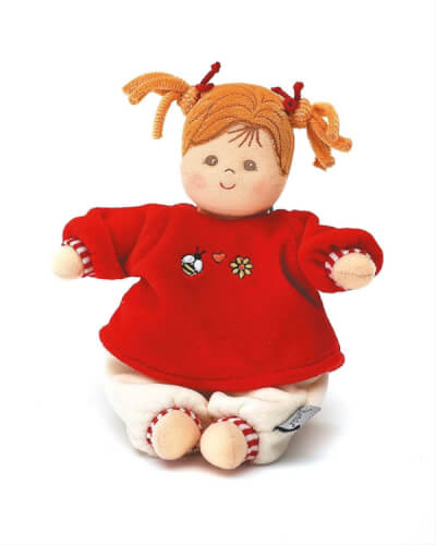 Das Bild zeigt eine weiche Stoffpuppe mit orangenen Zöpfen. Sie trägt ein rotes Oberteil mit Stickereien und weiße Hosen.