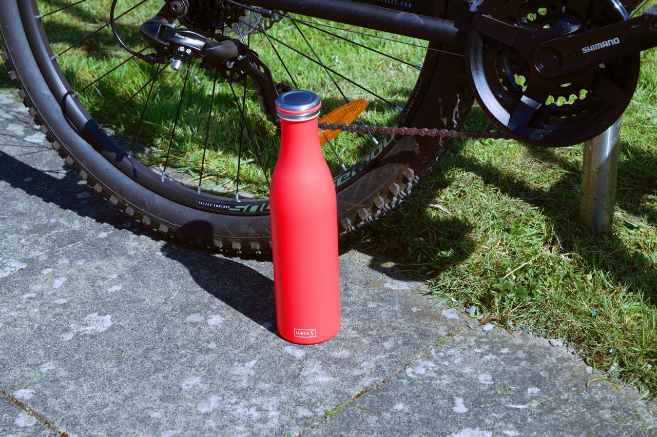 Auf dem Bild ist eine pinke Isolierflasche aus Edelstahl mit 0,75 Liter Fassungsvermögen zu sehen. Sie steht auf dem Gehweg neben einem Fahrrad.