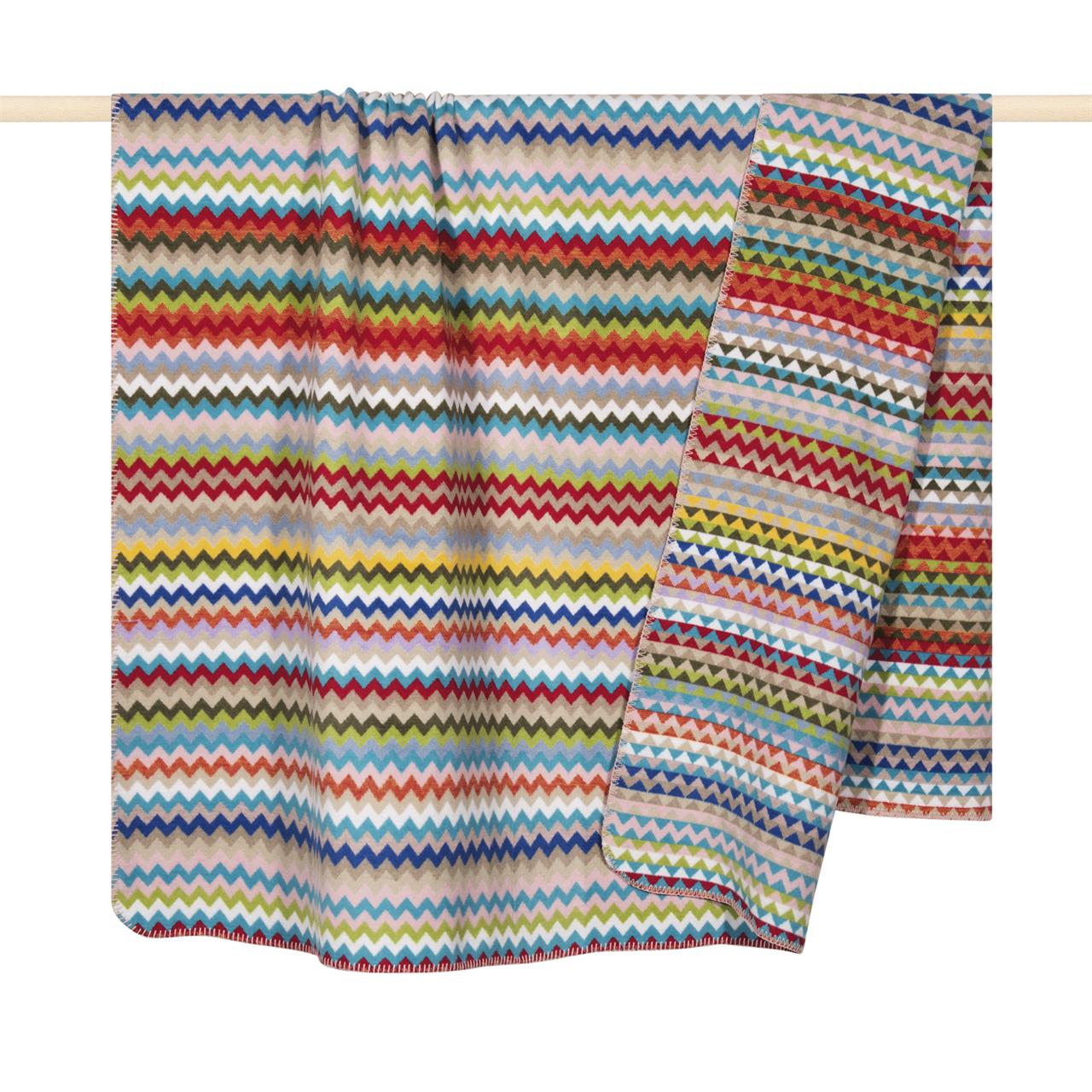 Die Decke "Celin" in der Größe 150x200 cm zeigt ein farbenfrohes Zickzackmuster in verschiedenen Farben. Sie besteht aus weichem Material und hat einen violetten Grundton.