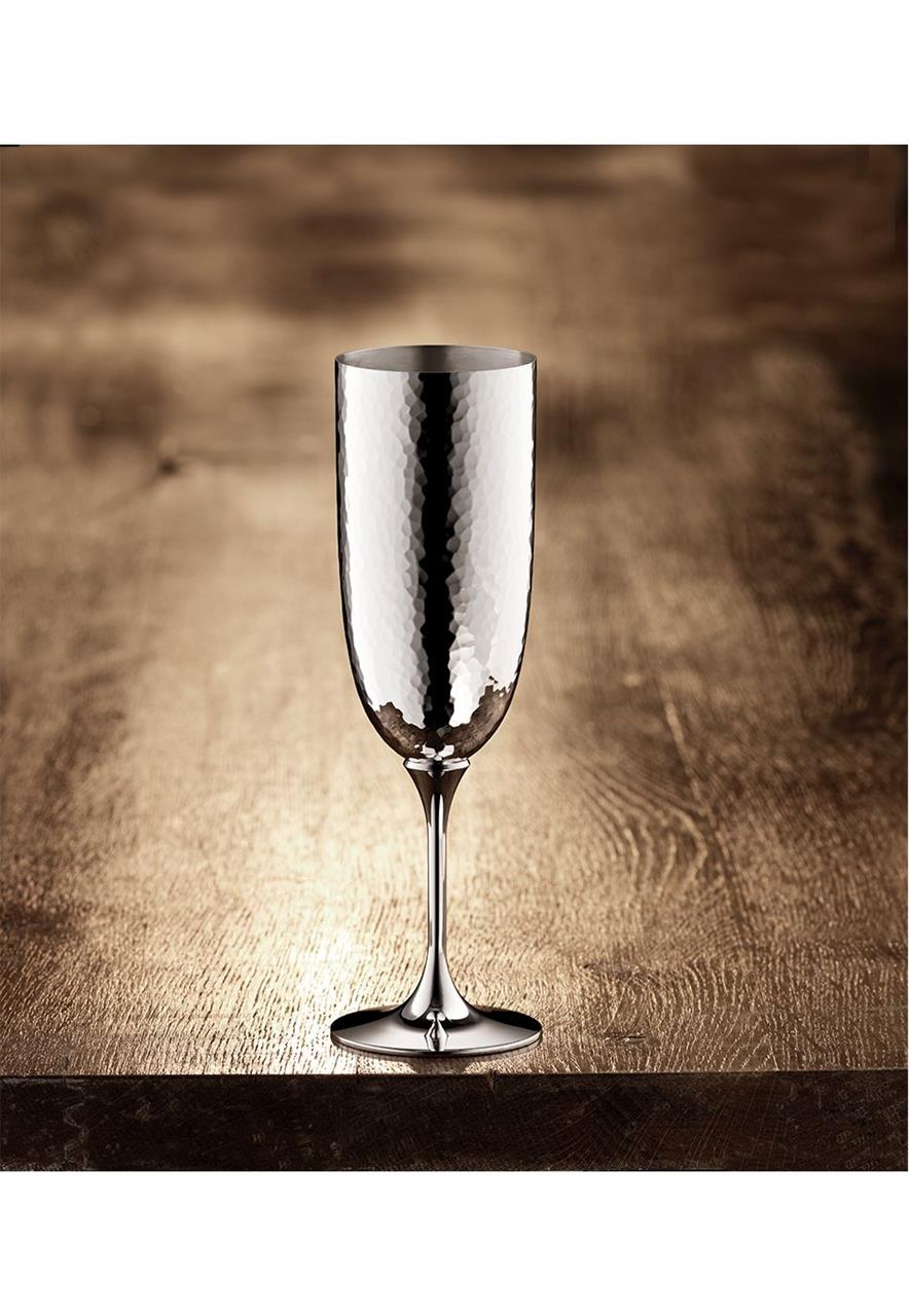 Dieses Bild zeigt den "Martelé 90 Champagnerkelch". Das elegante Sektglas besteht aus glänzendem, gehämmertem Metall und steht auf einem Holztisch.