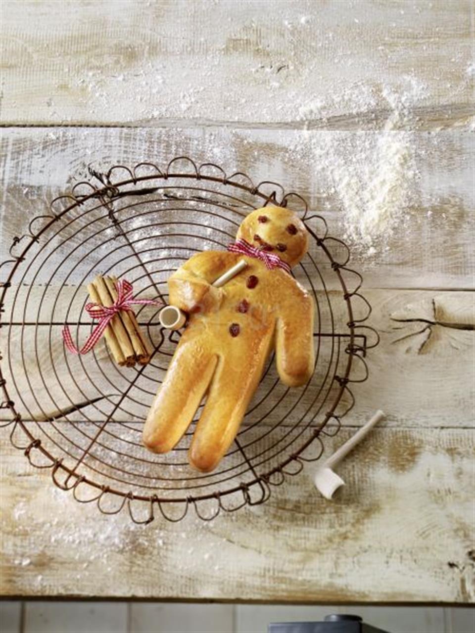 Auf dem Bild ist ein Stutenkerl, ein gebackener Teigmännchen, auf einem Kuchengitter zu sehen. Daneben liegen eine Zimtstange und eine kleine Pfeife aus Ton.