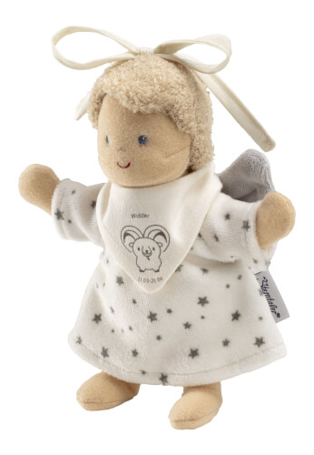 Auf dem Bild ist eine weiche Stoffpuppe mit Flügeln und einer Schleife auf dem Kopf zu sehen. Sie trägt ein weißes Kleid mit grauen Sternen und ein Lätzchen mit einem Widder-Motiv.