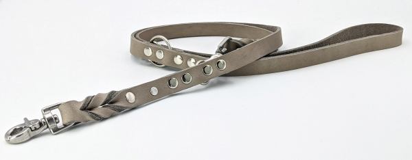 Auf dem Bild ist eine graue Hundeleine aus Leder mit Metallnieten und einem Karabinerhaken zu sehen. Die Leine liegt locker auf einem weißen Hintergrund.