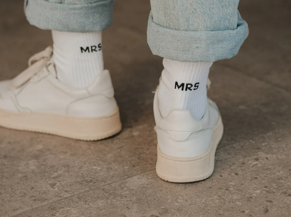 Abgebildet sind Socken mit der Aufschrift 'Mrs' in Größe M. Das Design ist schlicht und elegant gehalten.