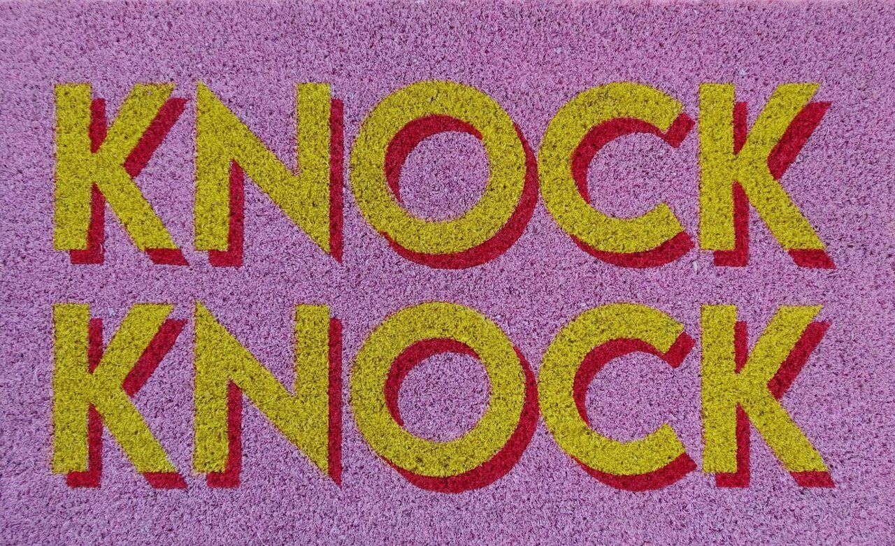 Gezeigt wird eine rosafarbene Fußmatte mit dem Motiv 'Knock Knock'. Sie sorgt für einen farbenfrohen Empfang im Zuhause.