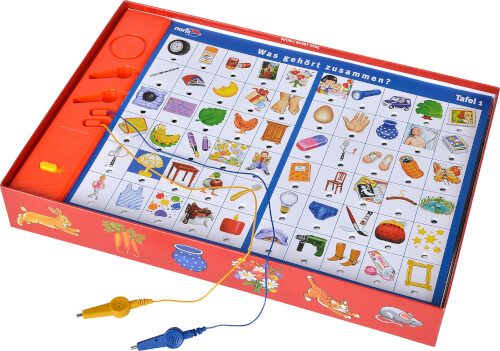 Das Bild zeigt ein Lernspiel mit vielen bunten Bildkarten, die in einem roten Karton angeordnet sind. Auf dem Spielbrett steht "Was gehört zusammen?" und es gibt Kabel mit Klemmen zum Verbinden der Paare.