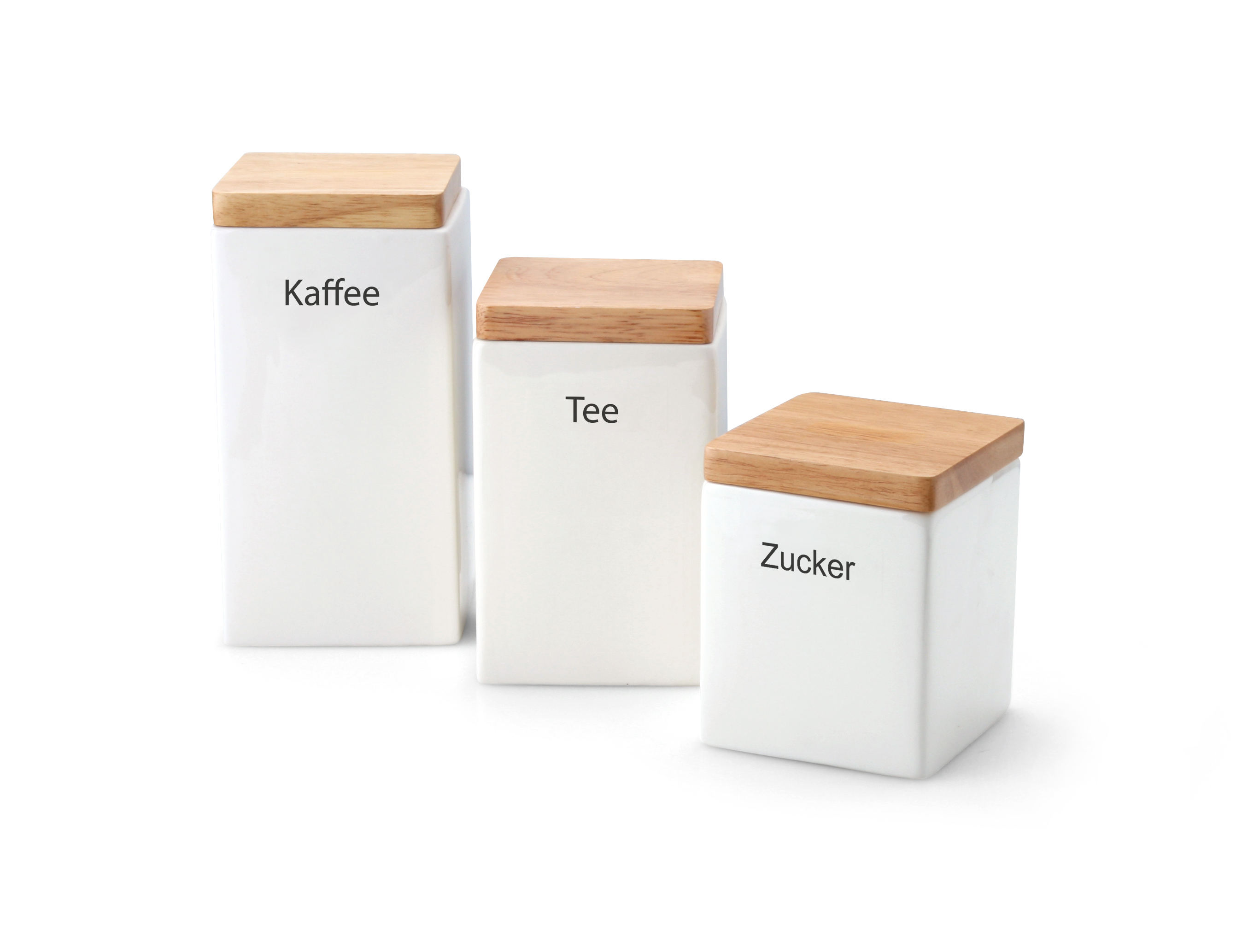 Auf dem Bild sind drei weiße Vorratsdosen mit Holzdeckeln zu sehen. Sie sind mit den deutschen Wörtern "Kaffee", "Tee" und "Zucker" beschriftet.