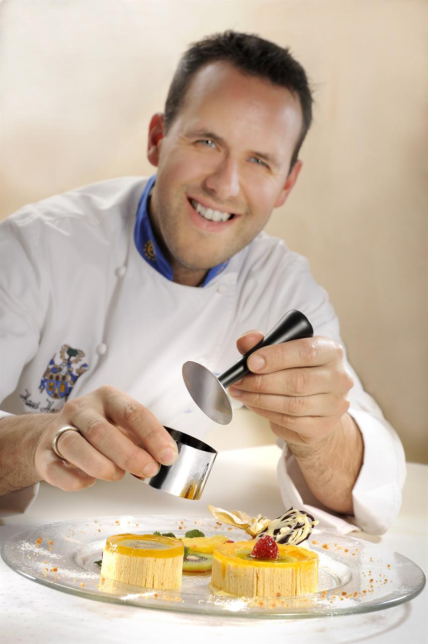 Ein Koch verwendet die Profispeisenringe Formidable, 10-tlg., um ein Dessert kunstvoll anzurichten. Auf dem Teller liegen dekorativ angerichtete Süßspeisen mit Früchten und Sauce.