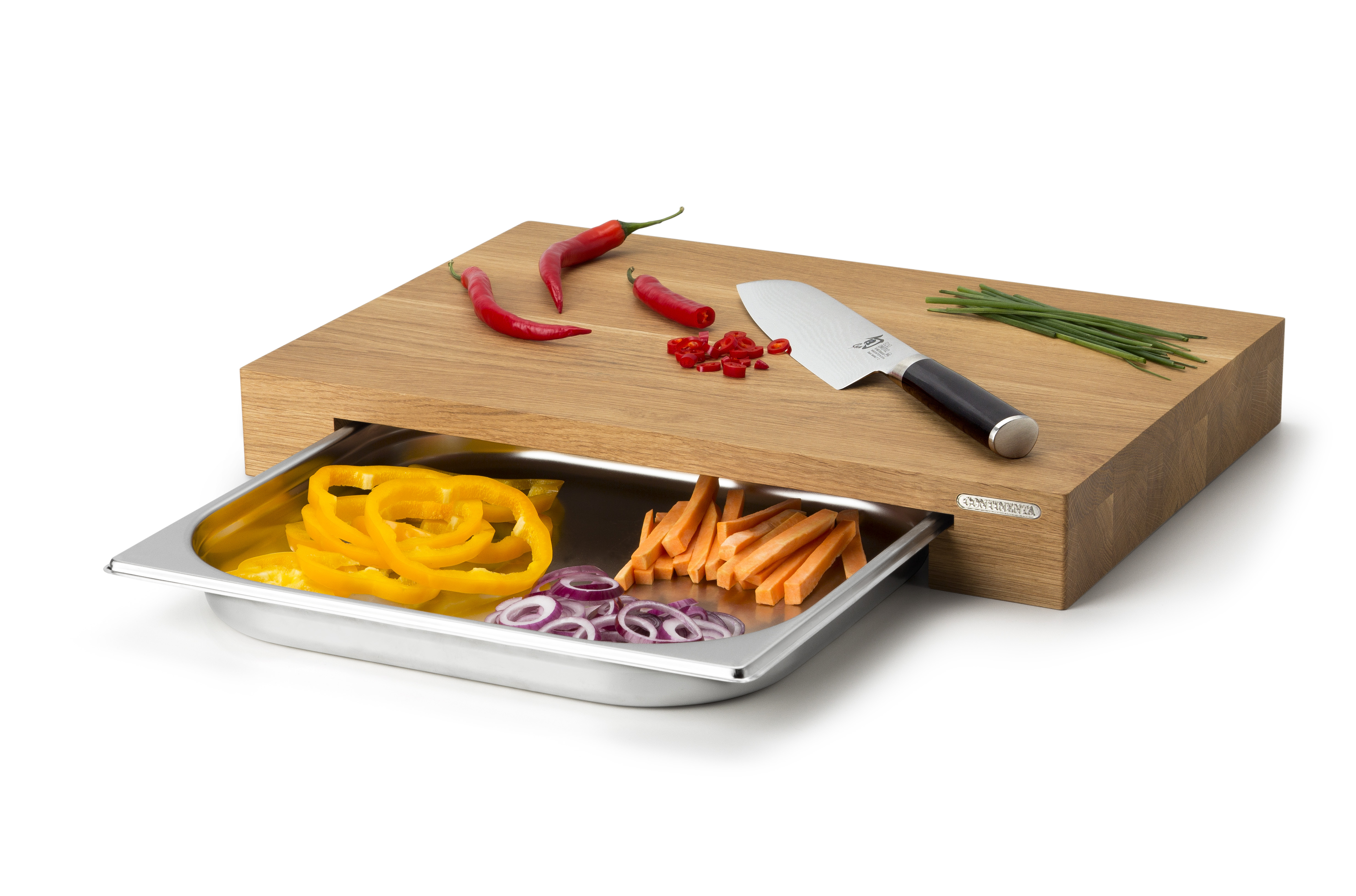 Auf dem Bild ist ein Holzschneidebrett mit einem Messer, Chilis und Schnittlauch zu sehen. Unter dem Brett befindet sich eine Metallschale mit geschnittenen Paprika, Karotten und roten Zwiebeln.