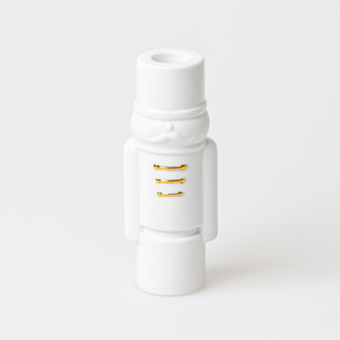 Die Figur auf dem Bild ist ein weißer Nussknacker mit goldenen Knöpfen. Sie hat eine zylindrische Form und steht aufrecht.