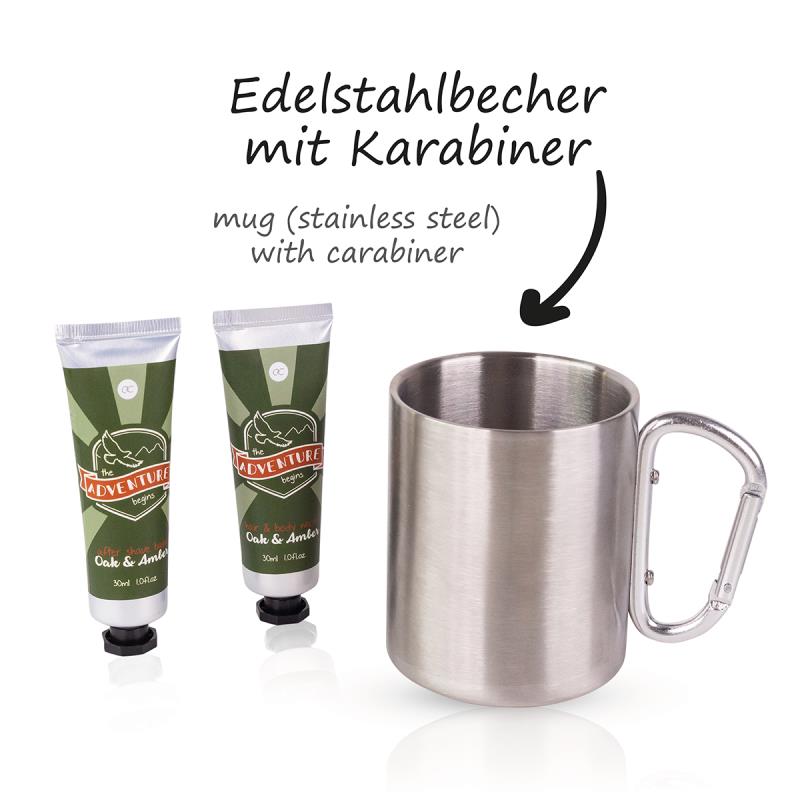Das Bild zeigt ein Badeset namens "Adventure Collection" mit einem Edelstahlbecher mit Karabiner. Neben dem Becher stehen zwei Tuben mit Pflegeprodukten.