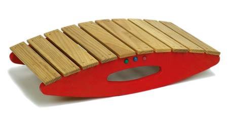 Das Bild zeigt eine Balance-Schaukel aus Holz mit seitlichen roten Wangen. Die Oberseite besteht aus mehreren parallel angeordneten Holzlatten.