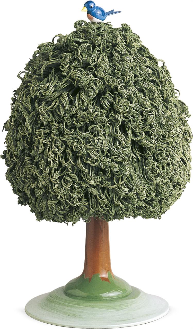 Das Bild zeigt einen dekorativen Laubbaum mit dichtem grünem Laub aus Garn. Auf der Spitze des Baumes sitzt ein kleiner, blauer Vogel.