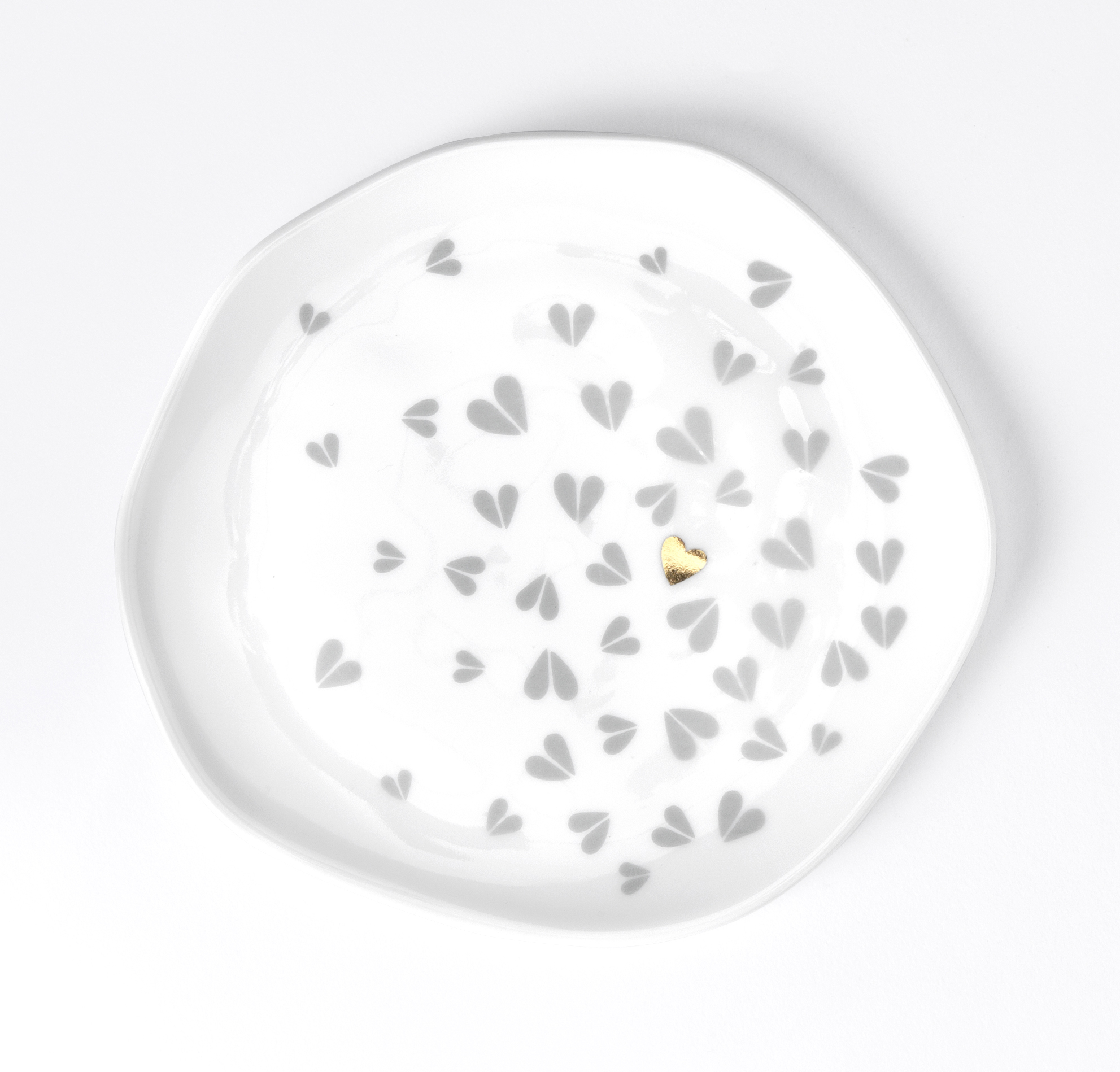 Der kleine weiße Teller hat ein Muster aus grauen Herzen und ein einzelnes goldenes Herz in der Mitte. Das Design wirkt zart und liebevoll.