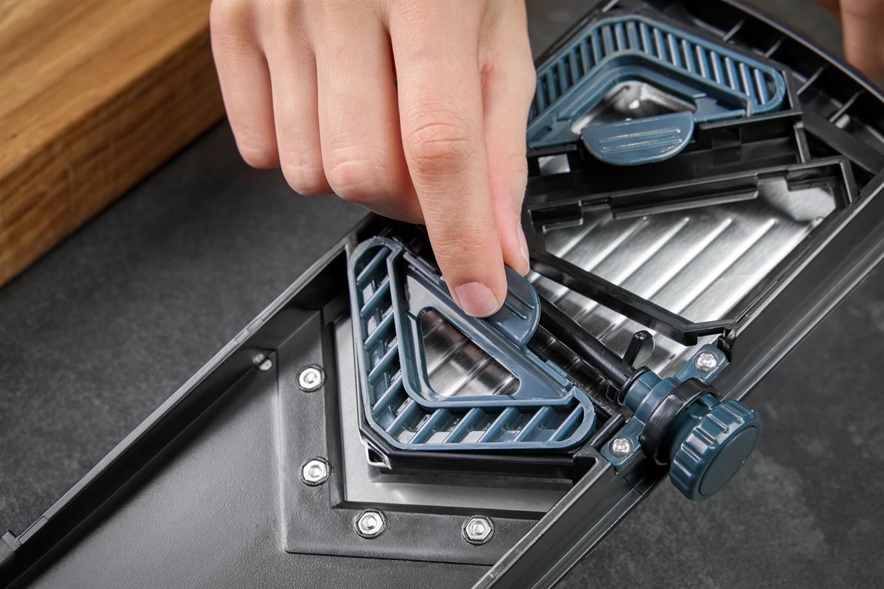 Auf dem Bild ist eine Hand zu sehen, die an einem V-Hobel Julienne Collect einstellt. Das Küchengerät wird zum präzisen Schneiden von Gemüse verwendet.