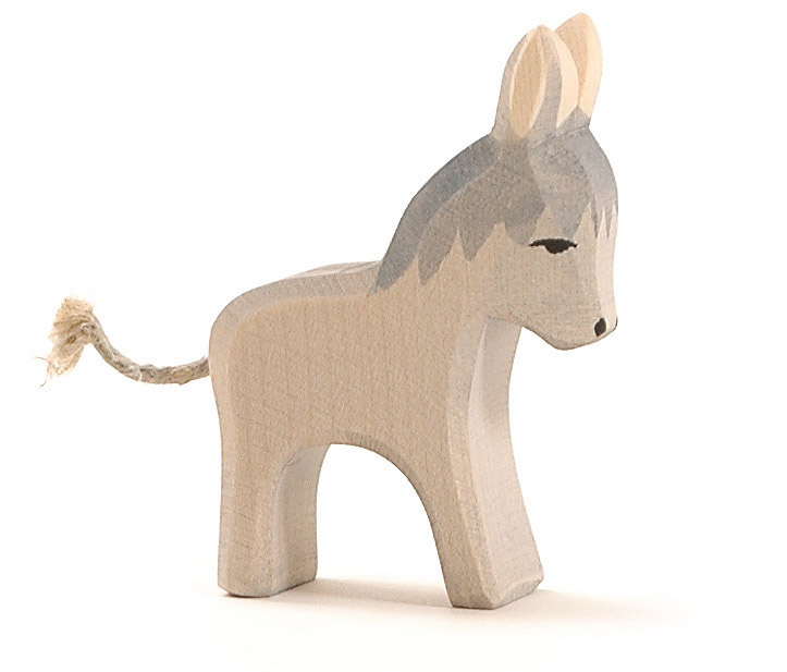 Das Bild zeigt eine kleine, handgefertigte Holzfigur in Form eines Esels. Die Figur hat einen grauen Rücken und einen Schwanz aus Schnur.