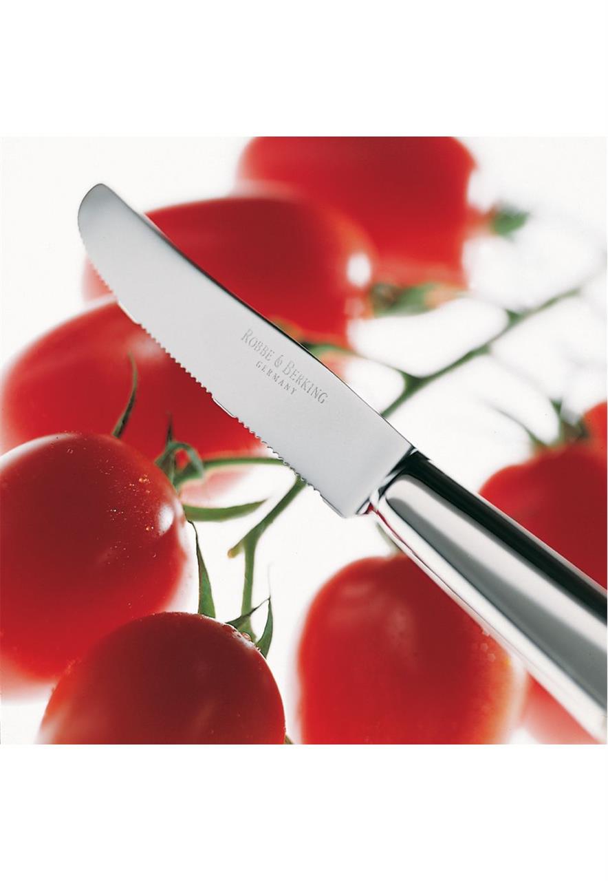 Das Bild zeigt ein silbernes Tomatenmesser namens "Dante 925 Tomatenmesser" vor mehreren frischen Tomaten. Das Messer hat eine gezackte Klinge und einen glänzenden Griff.