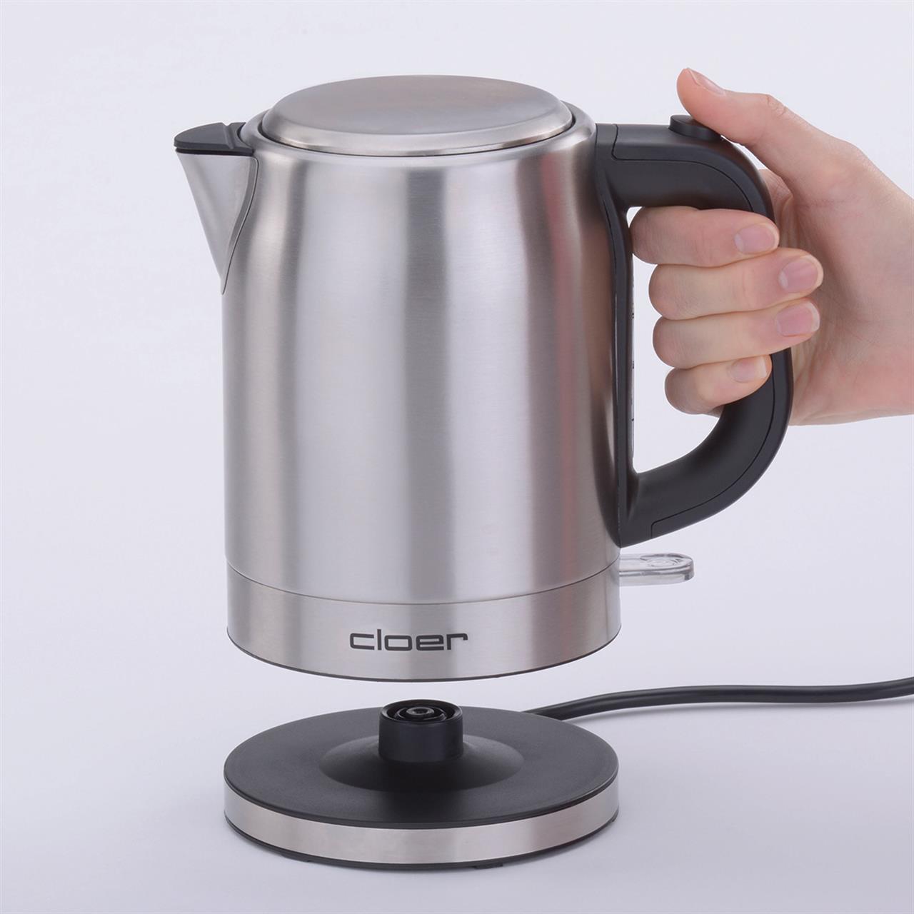 Der Wasserkocher Inox 1,0L Cloer 4519 wird von einer Hand am Griff gehalten. Das Gerät besteht aus Edelstahl und steht über einer runden Basisstation.