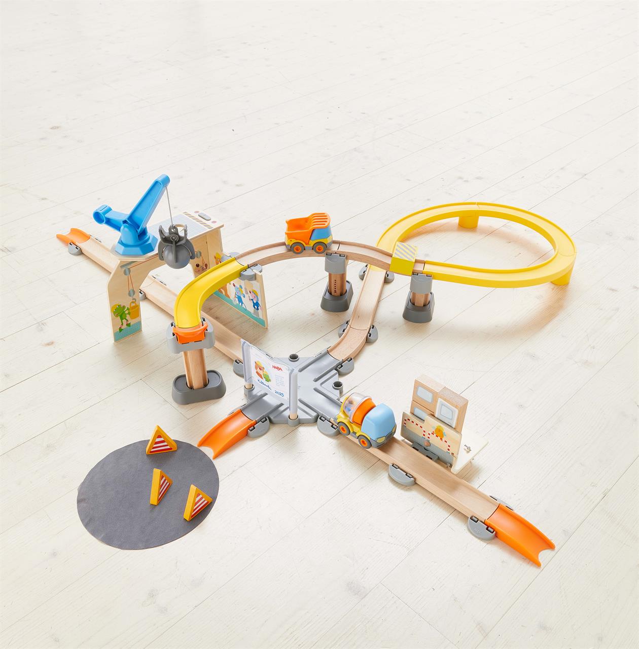 Das Bild zeigt das Spielset "Kullerbü – Spielbahn: Große Baustelle" aufgebaut auf einem hellen Holzboden. Zu sehen sind bunte Schienen, Fahrzeuge, Baustellenzubehör und verschiedene Spielstationen.