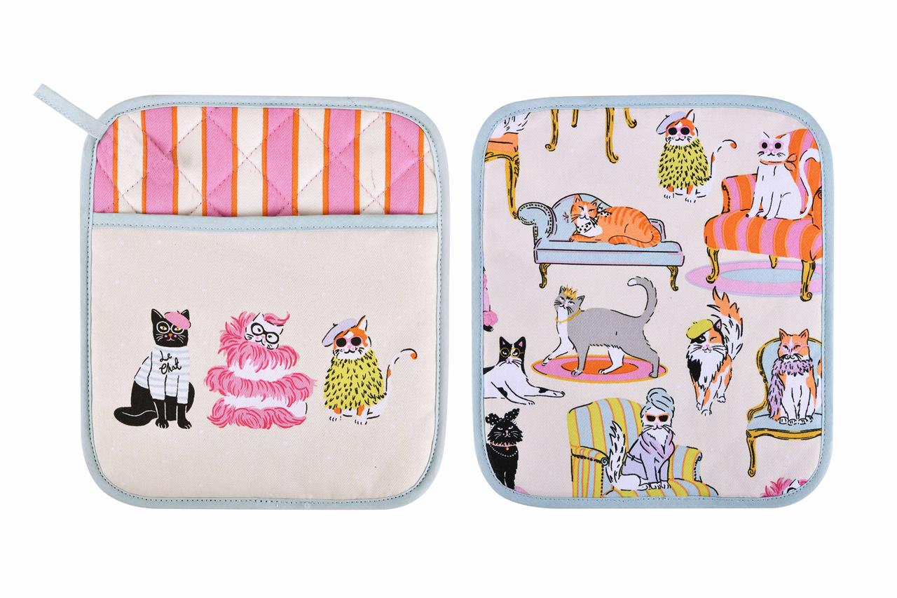 Das Bild zeigt zwei bunte Topflappen mit lustigen Katzenmotiven. Die Katzen sind kreativ und modisch gezeichnet und sitzen auf stilvollen Möbeln.
