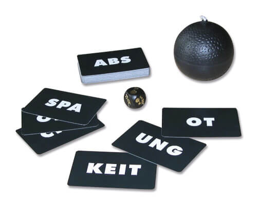 Auf dem Bild sind mehrere schwarze Karten mit weißen Buchstaben, ein Würfel und eine schwarze Kugel zu sehen. Die Karten zeigen Wortbestandteile wie "ABS", "UNG", "KEIT" und "OT".