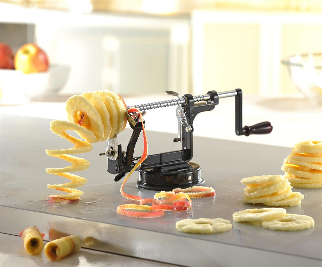 Das Bild zeigt den Apfelschäler Delicio 3 in 1, der einen Apfel spiralförmig schält und schneidet. Um den Schäler liegen mehrere, in Scheiben geschnittene und geschälte Apfelstücke.