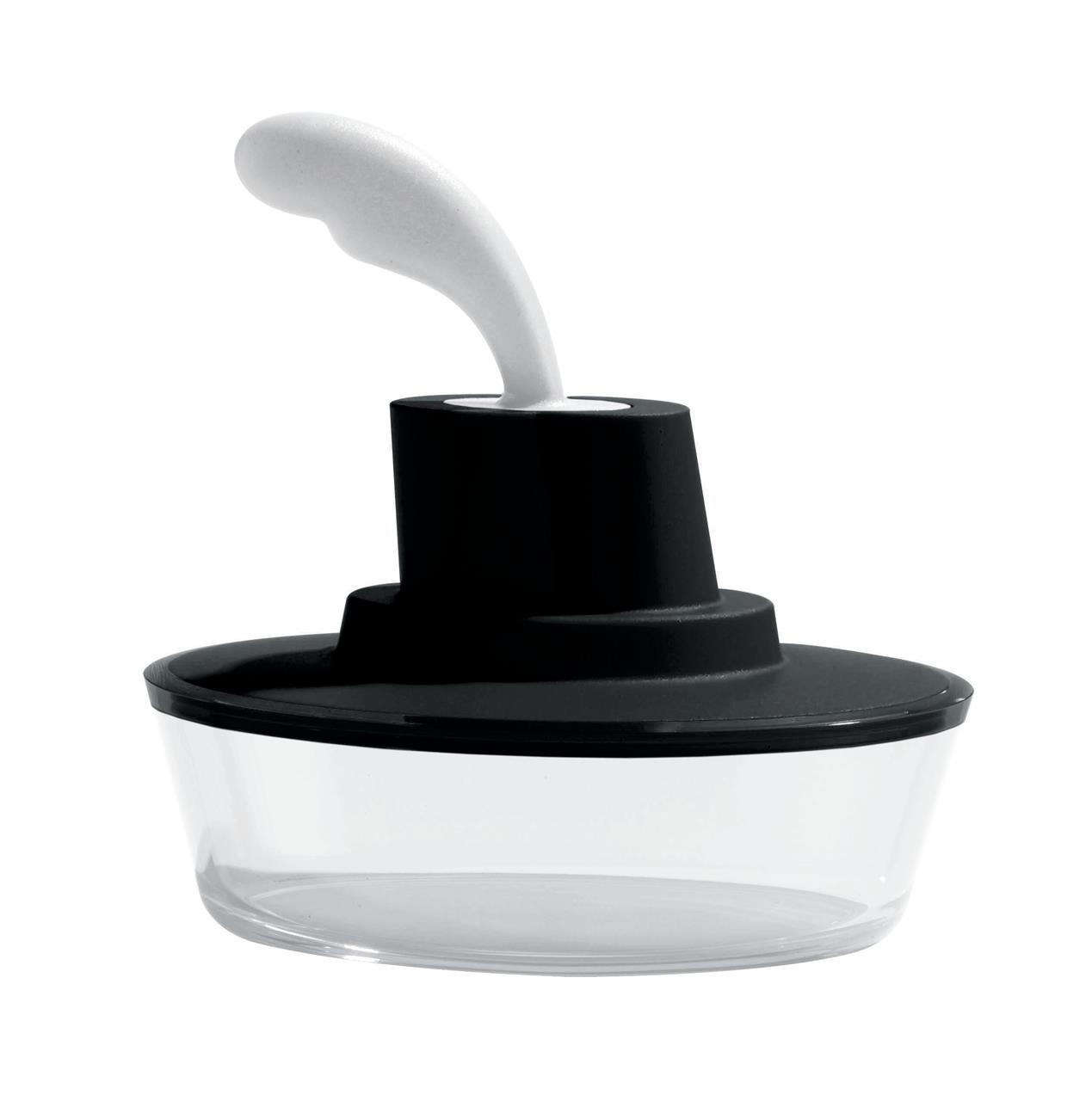 Die Butterdose "Ship Shape" hat die Form eines kleinen Schiffes. Sie besteht aus transparentem Glas mit einem schwarzen Deckel und einem weißen Griff.